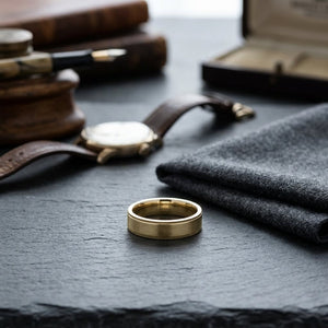 6mm Flat Milgrain Comfort-Fit Wedding Band in 18K Yellow Gold, on walnut surface with pocket square