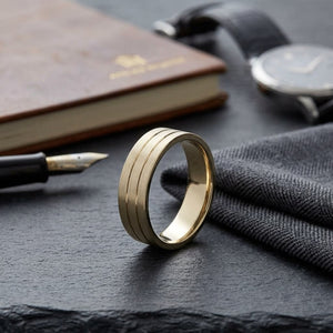 6mm Satin Finish Parallel Center Cut Carved Wedding Band in 18K Yellow Gold, on walnut surface with pocket square