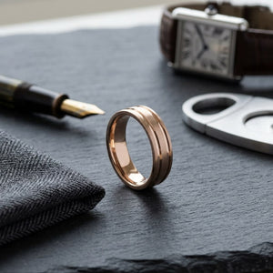 6mm Satin Finish Parallel Groove Carved Wedding Band in 14K Rose Gold, on walnut surface with pocket square
