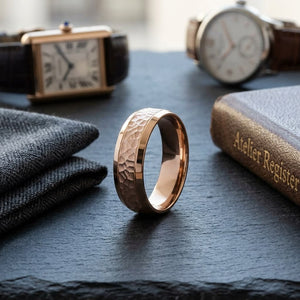 7.5mm Hammered Finish Beveled Edge Carved Wedding Band in 14K Rose Gold, on walnut surface with pocket square