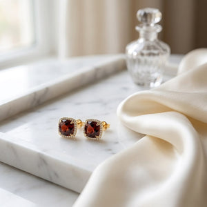 Garnet Cushion Stud Earrings in 14K Yellow Gold, on marble vanity tray with silk