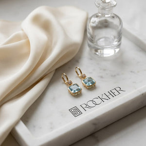 Swiss Blue Topaz Bezel Earrings in 14k Yellow Gold 0.08ctw, on marble vanity tray with silk