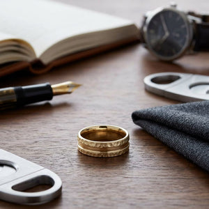 7.5mm Hammered Finish Carved Wedding Band in 14K Yellow Gold, on walnut surface with pocket square