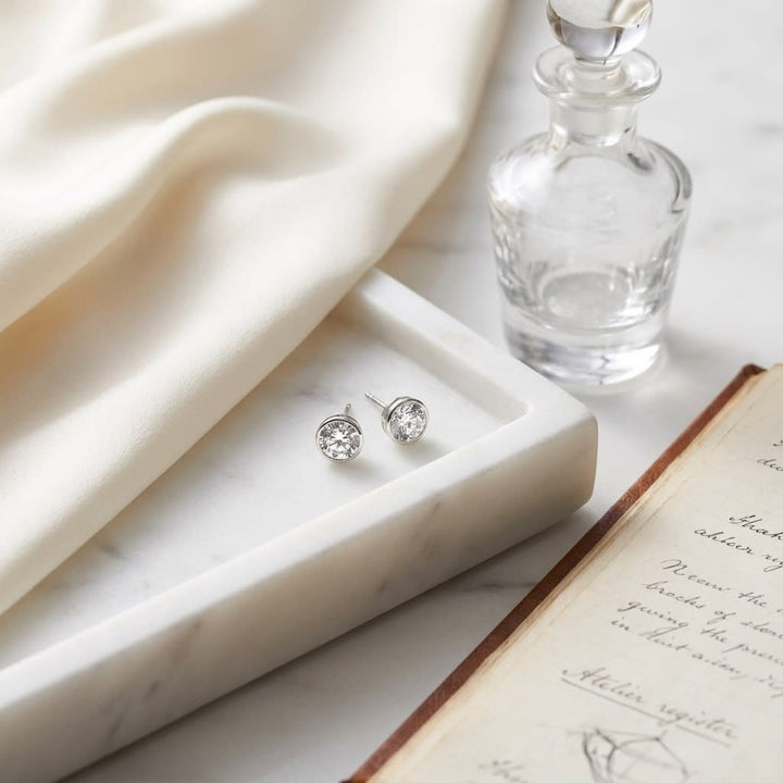 Platinum Bezel Set Round Brilliant Diamond Stud Earrings (0.75 Ct. T.w., Si1-si2 Clarity, J-k Color), on marble vanity tray with silk