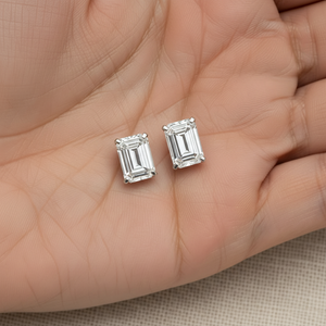Emerald cut lab diamond stud earrings held in hand, platinum, scale reference