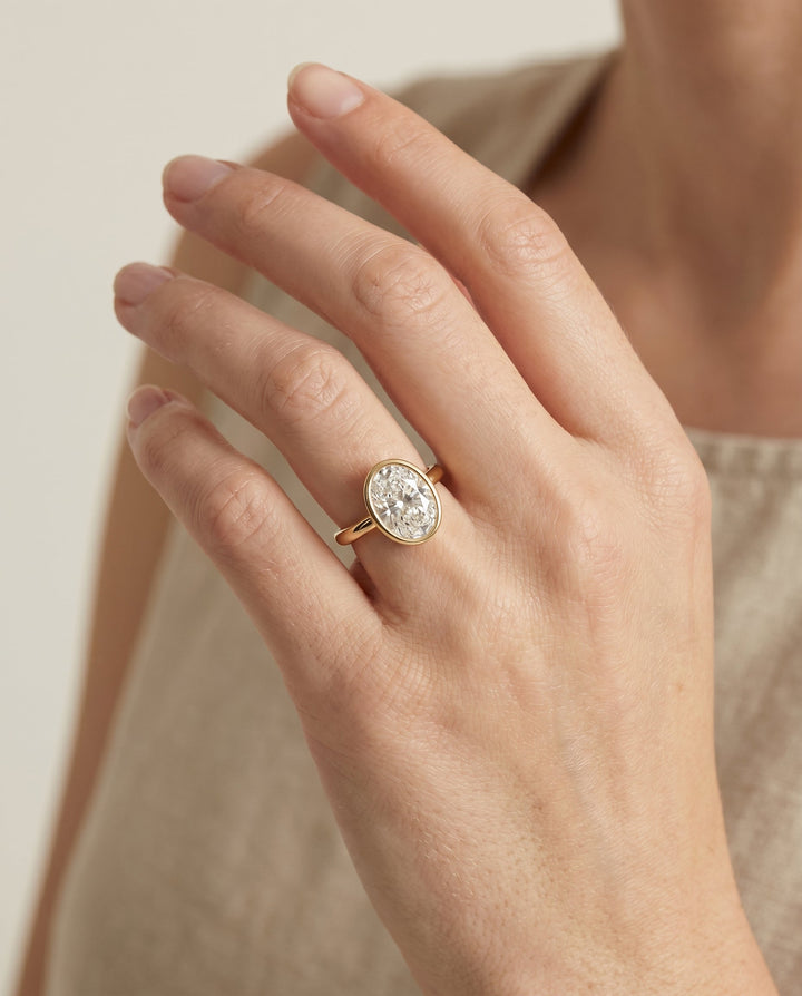 Agnes Select Bezel Solitaire In Oval Lab Diamond Engagement Ring in 18K Yellow Gold, shown on hand | RockHer