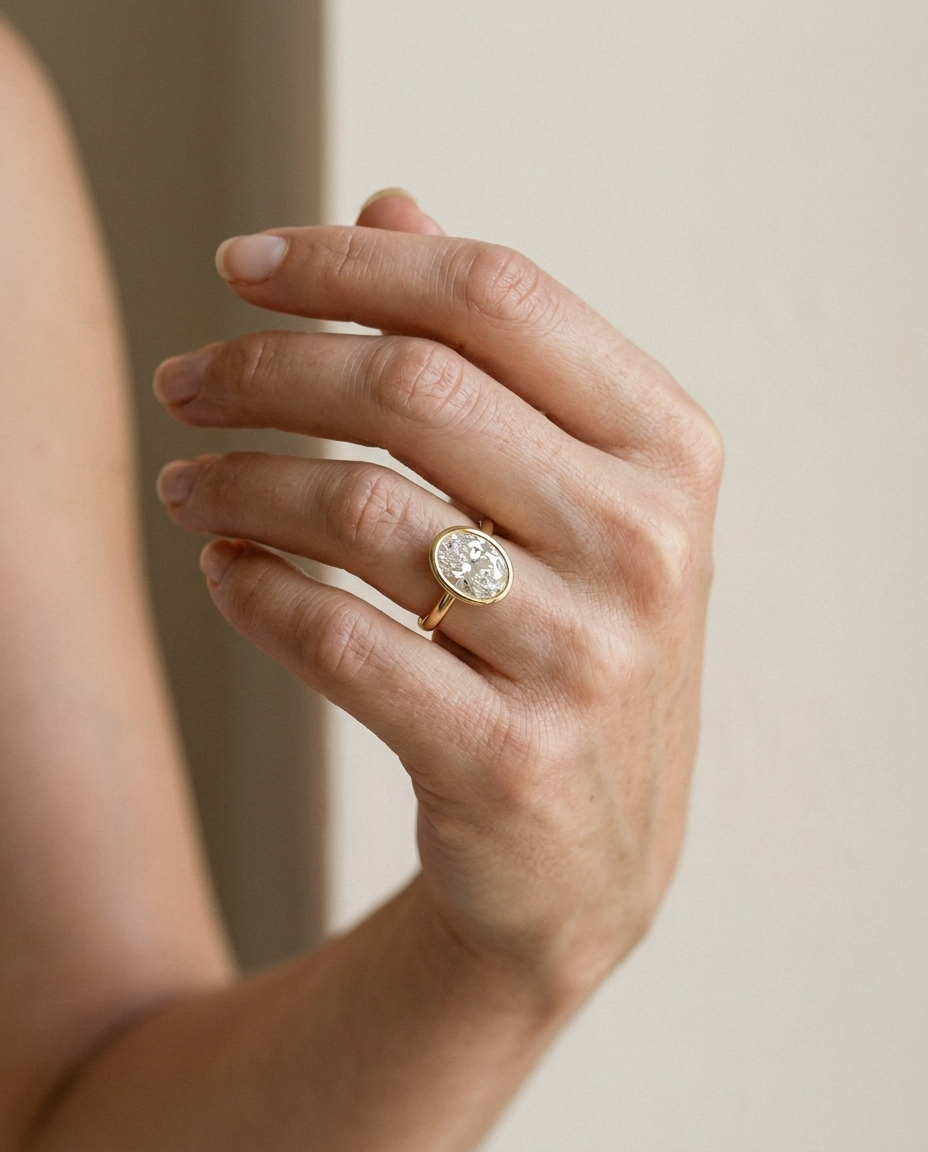 The Agnes Select bezel solitaire oval engagement ring in 18k yellow gold — on hand — RockHer