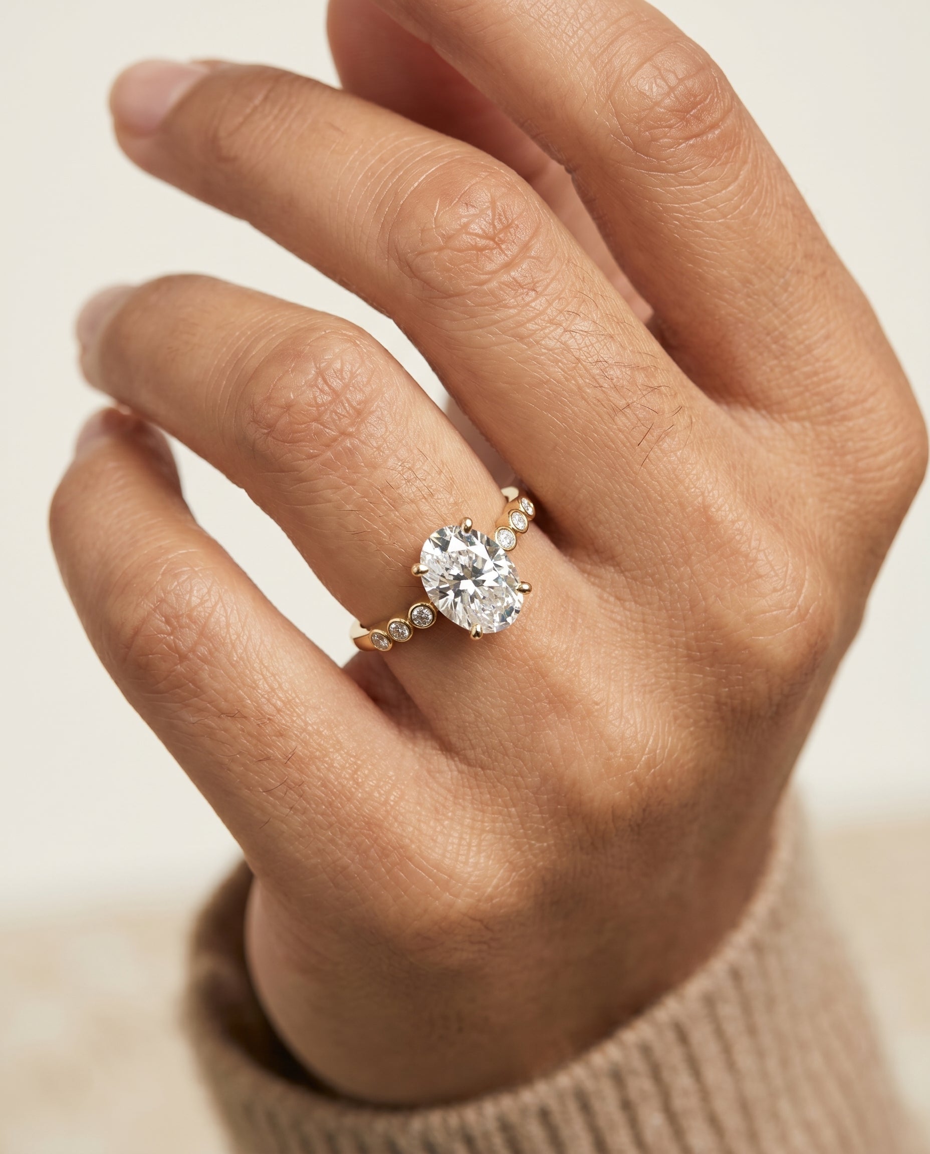 Peggy Select Bezel Accent Solitaire Oval Lab Diamond Engagement Ring in 18K Yellow Gold, shown on hand, angled | RockHer
