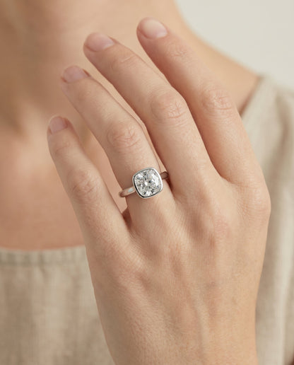 Duran Select Simple Bezel Solitaire Cushion Cut Lab Diamond Engagement Ring in Platinum, shown on hand | RockHer