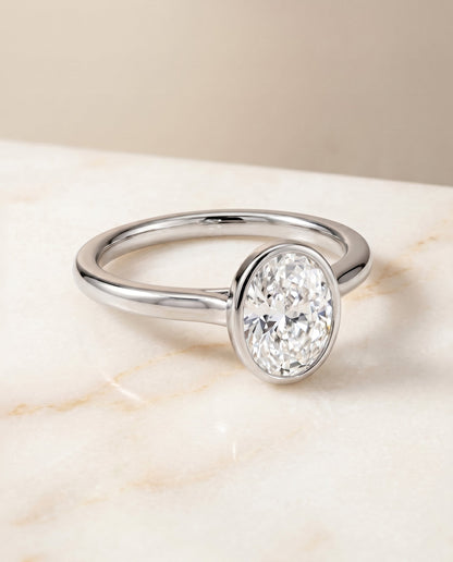 Duran Select Simple Bezel Solitaire Oval Lab Diamond Engagement Ring in Platinum, shown on hand, angled | RockHer