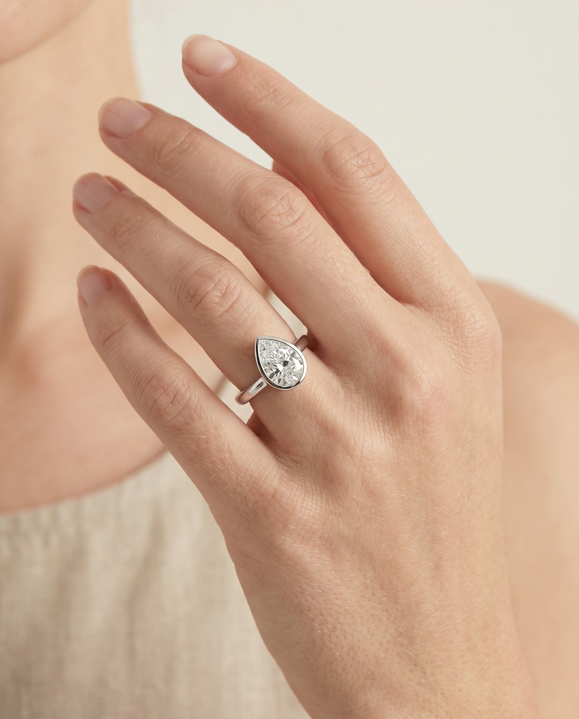 Duran Select Simple Bezel Solitaire Pear Lab Diamond Engagement Ring in Platinum, shown on hand | RockHer