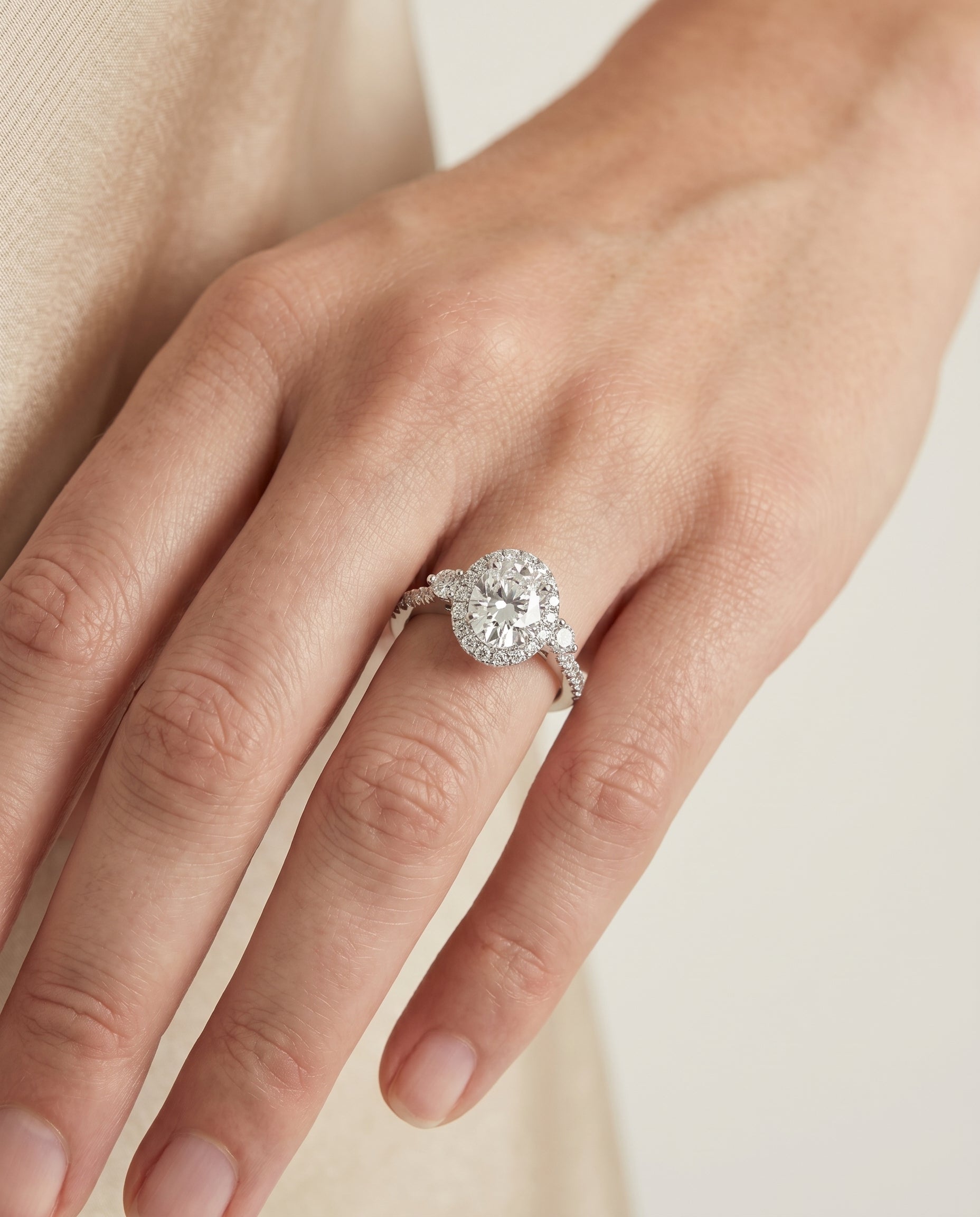 Ivy Select Three Stone Delicate Halo Oval Lab Diamond Engagement Ring in Platinum, shown on hand, angled | RockHer
