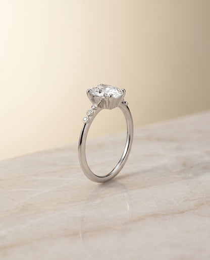Peggy Select Bezel Accent Solitaire Oval Lab Diamond Engagement Ring in 18K White Gold, shown on hand, angled | RockHer