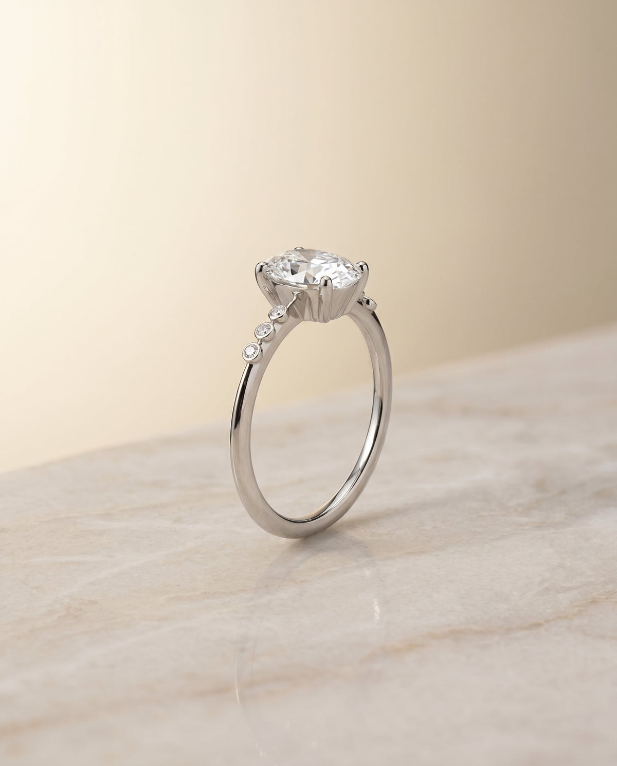 Peggy Select Bezel Accent Solitaire Oval Lab Diamond Engagement Ring in Platinum, shown on hand, angled | RockHer