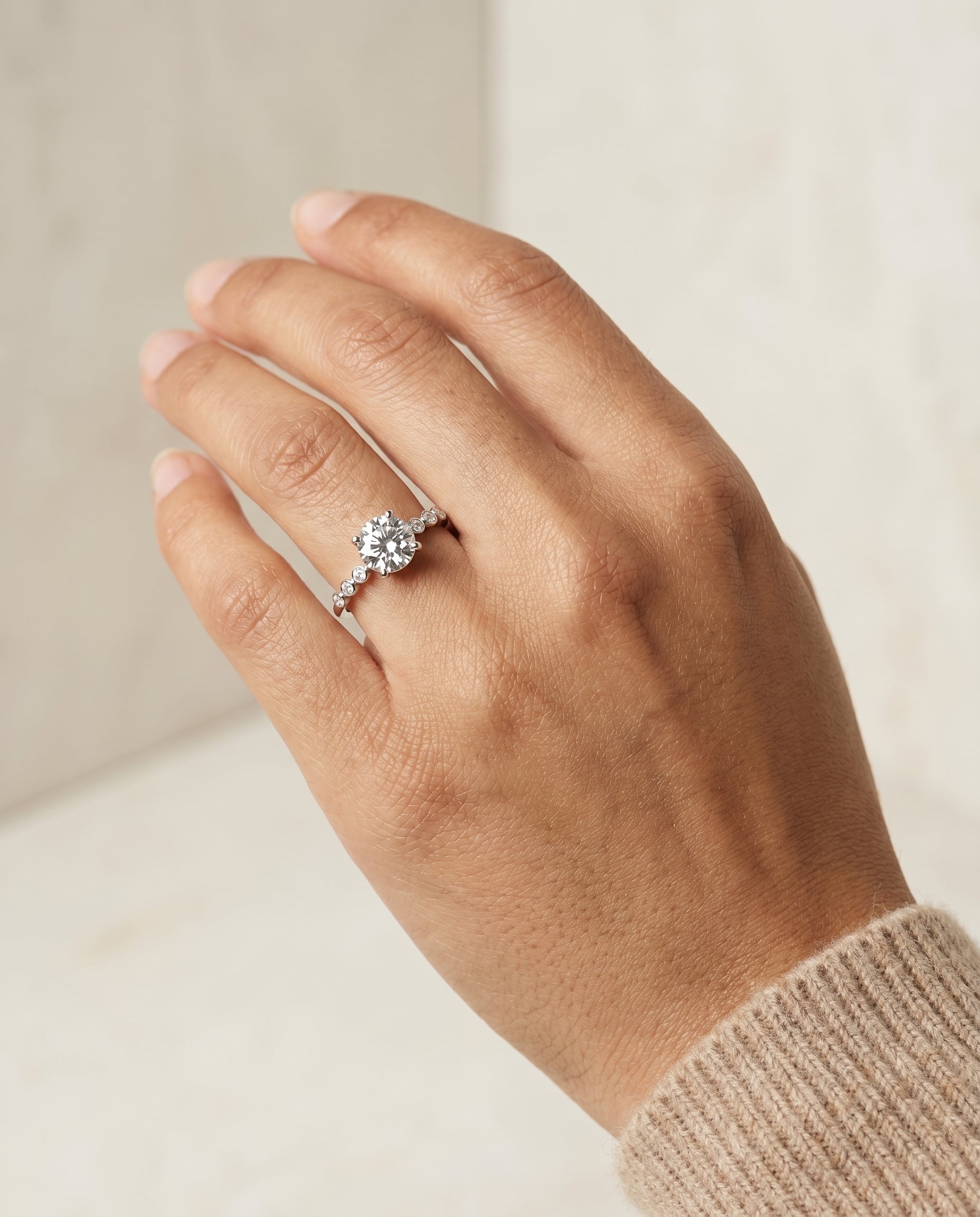 Peggy Select Bezel Accent Solitaire Round Lab Diamond Engagement Ring in 18K White Gold, shown on hand, angled | RockHer
