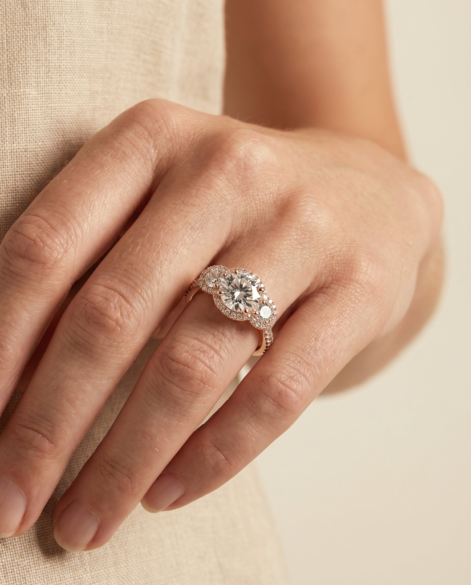 Andrea Select Three Stone Halo Round Lab Diamond Engagement Ring in 14K Rose Gold, shown on hand, angled | RockHer